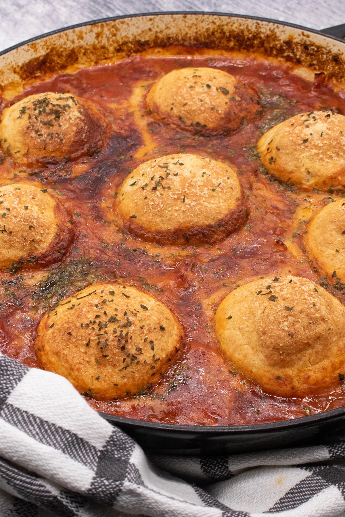 Chicken arrabbiata stew and parmesan dumplings in round casserole dish with black and white towel