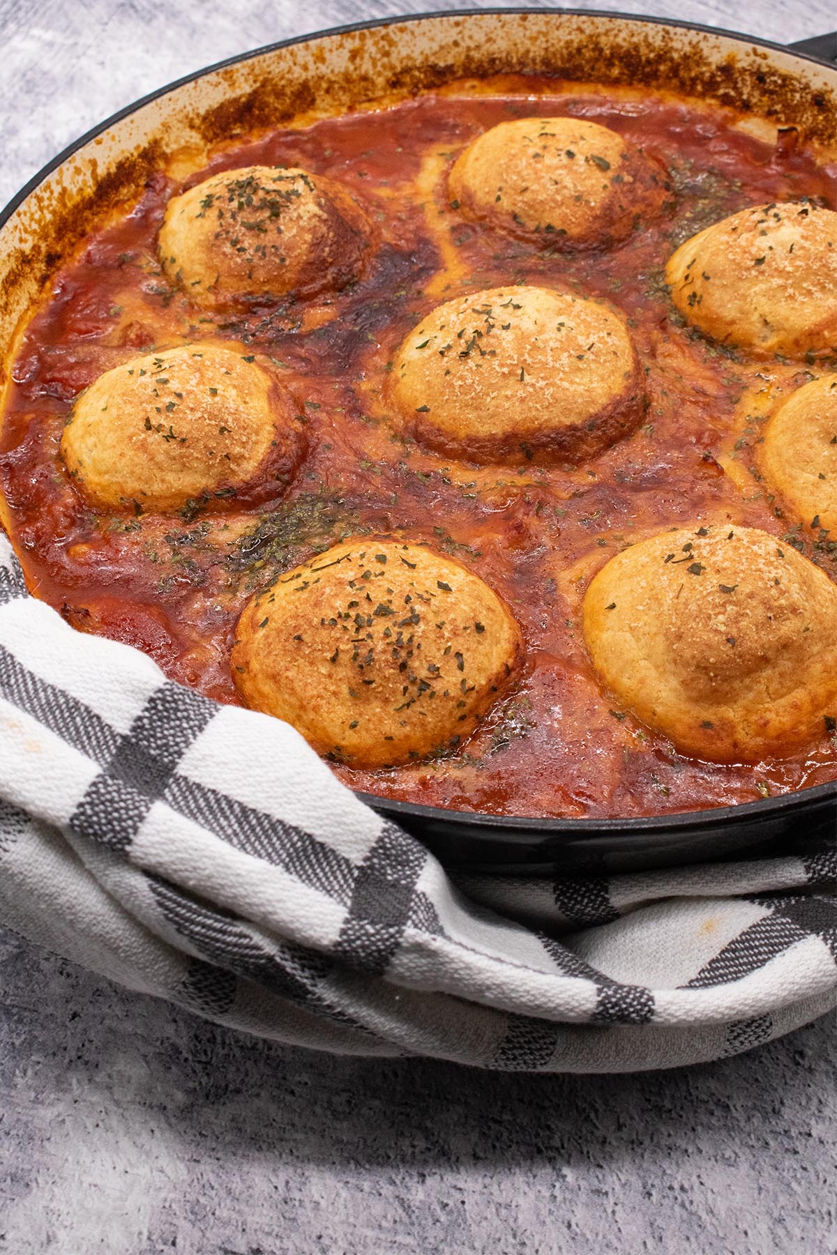 Chicken arrabbiata stew and parmesan dumplings in round casserole dish with black and white towel