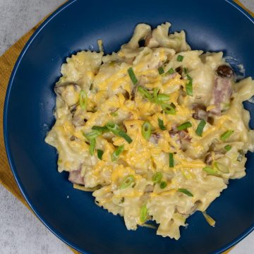 Creamy ham and mushroom pasta bake in a dark blue bowl sitting on a mustard napkin
