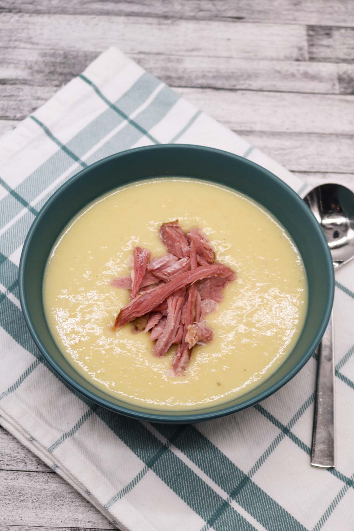 Creamy leek and potato soup in green bowl topped with ham