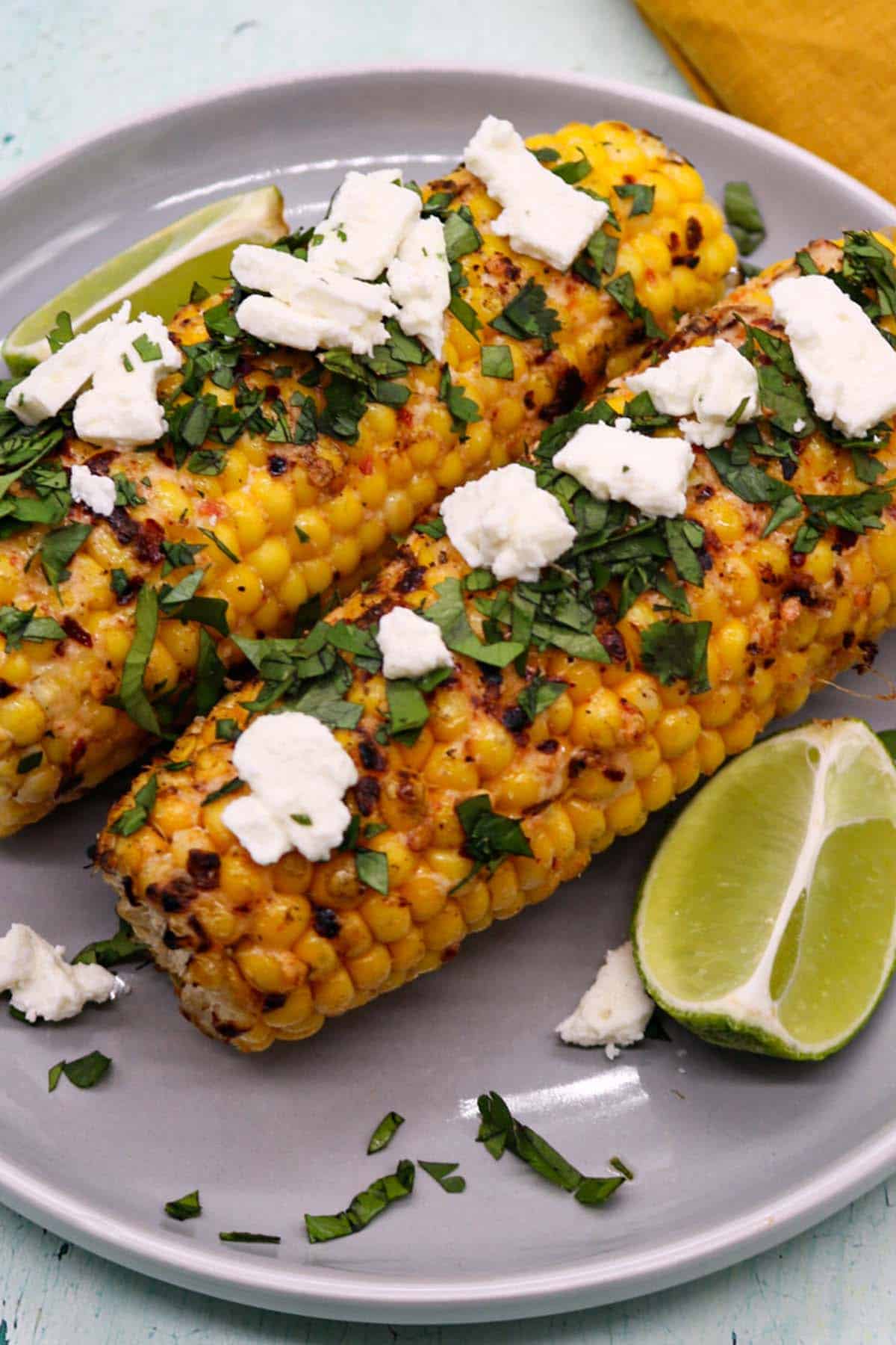 Grilled corn with feat coriander and lime wedges on grey plate