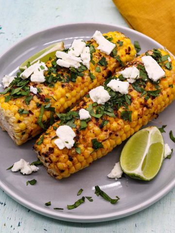Grilled corn with feat coriander and lime wedges on grey plate