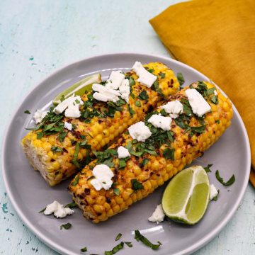 Grilled corn with feat coriander and lime wedges on grey plate