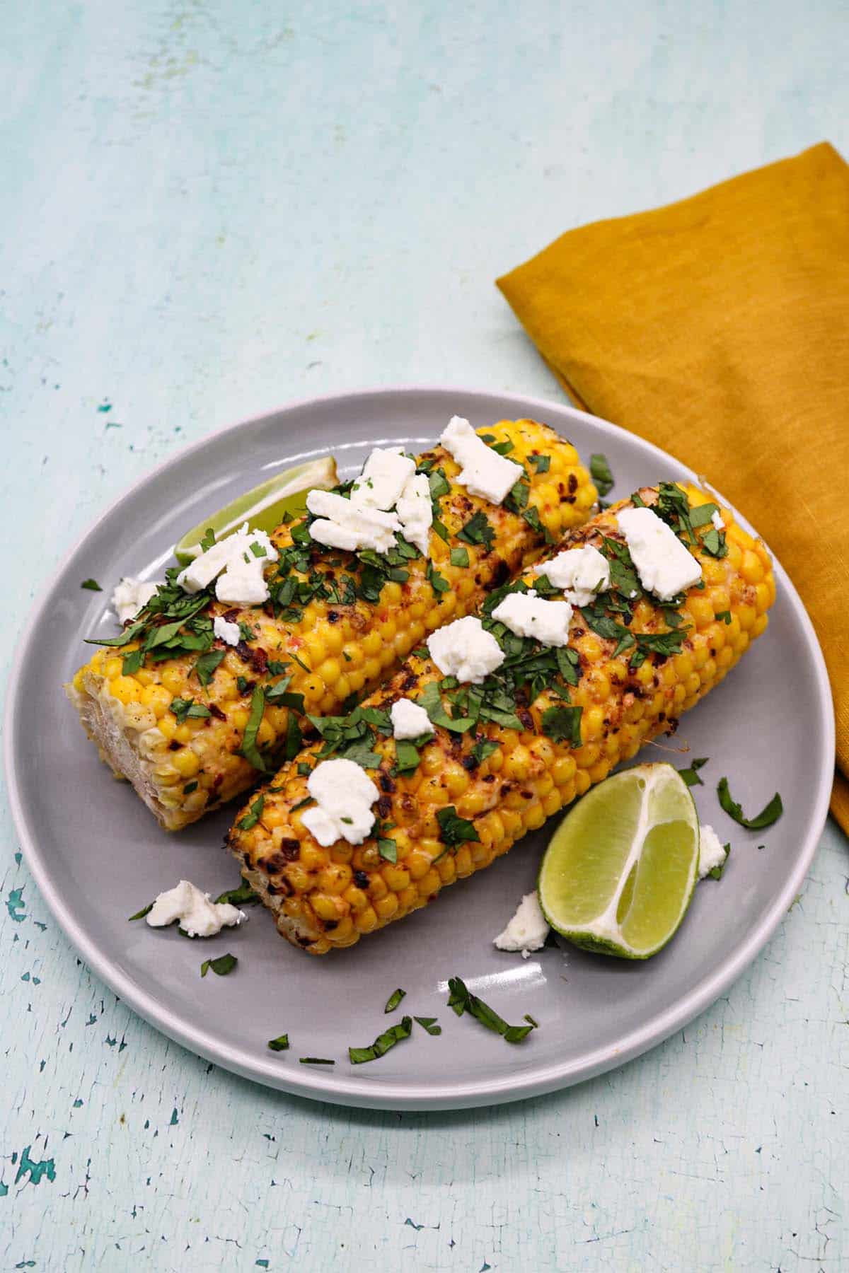 Grilled corn with feat coriander and lime wedges on grey plate