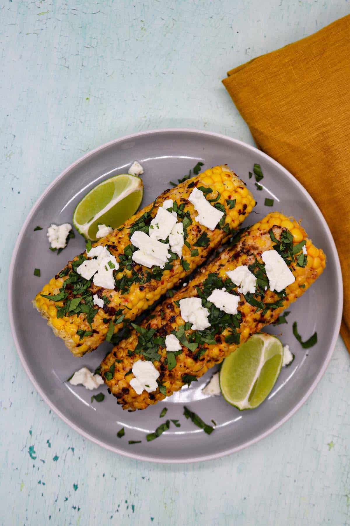 Grilled corn with feat coriander and lime wedges on grey plate