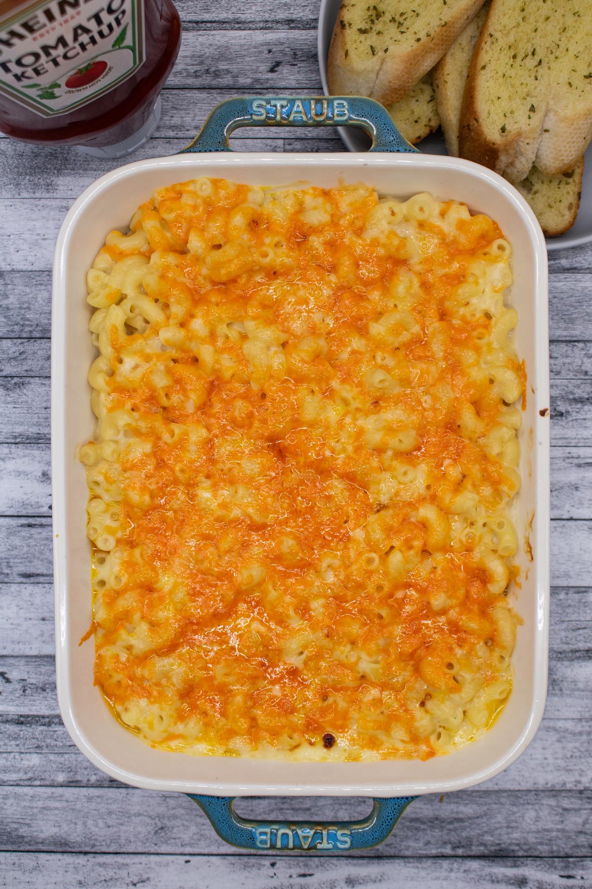 Macaroni cheese in rectangle dish next to garlic bread slices and tomato ketchup