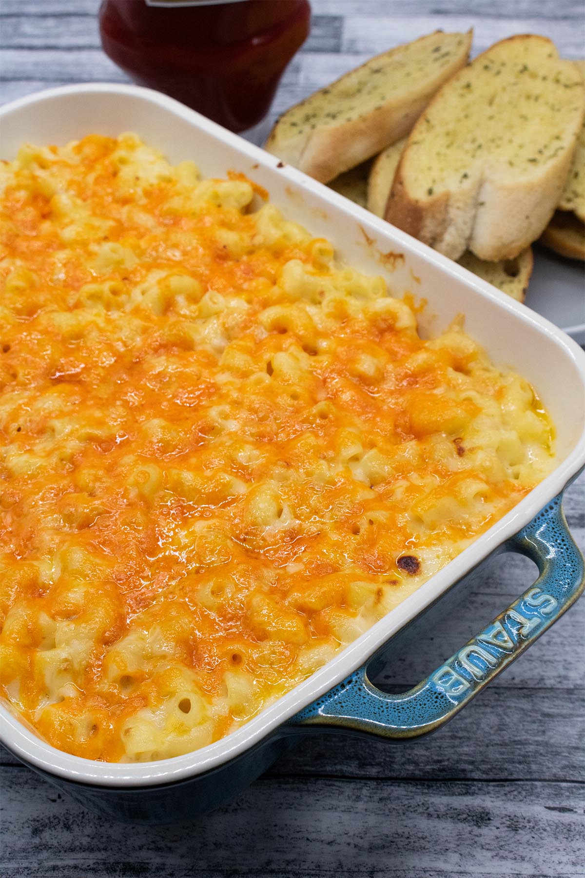 Macaroni cheese in rectangle dish next to garlic bread slices
