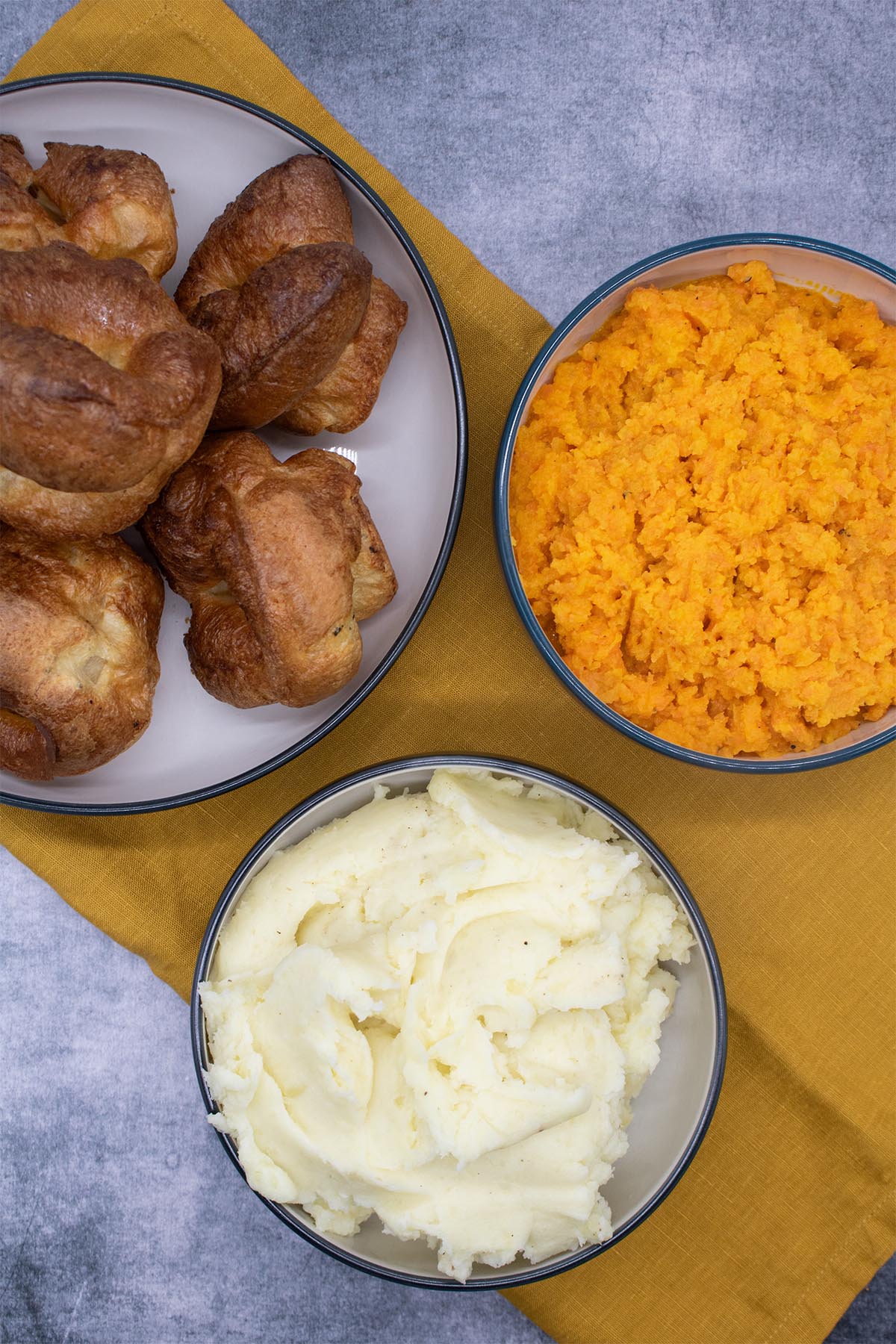 carrot and swede mash, mashed potatoes and yorkshire puddings in bowls with orange napkin