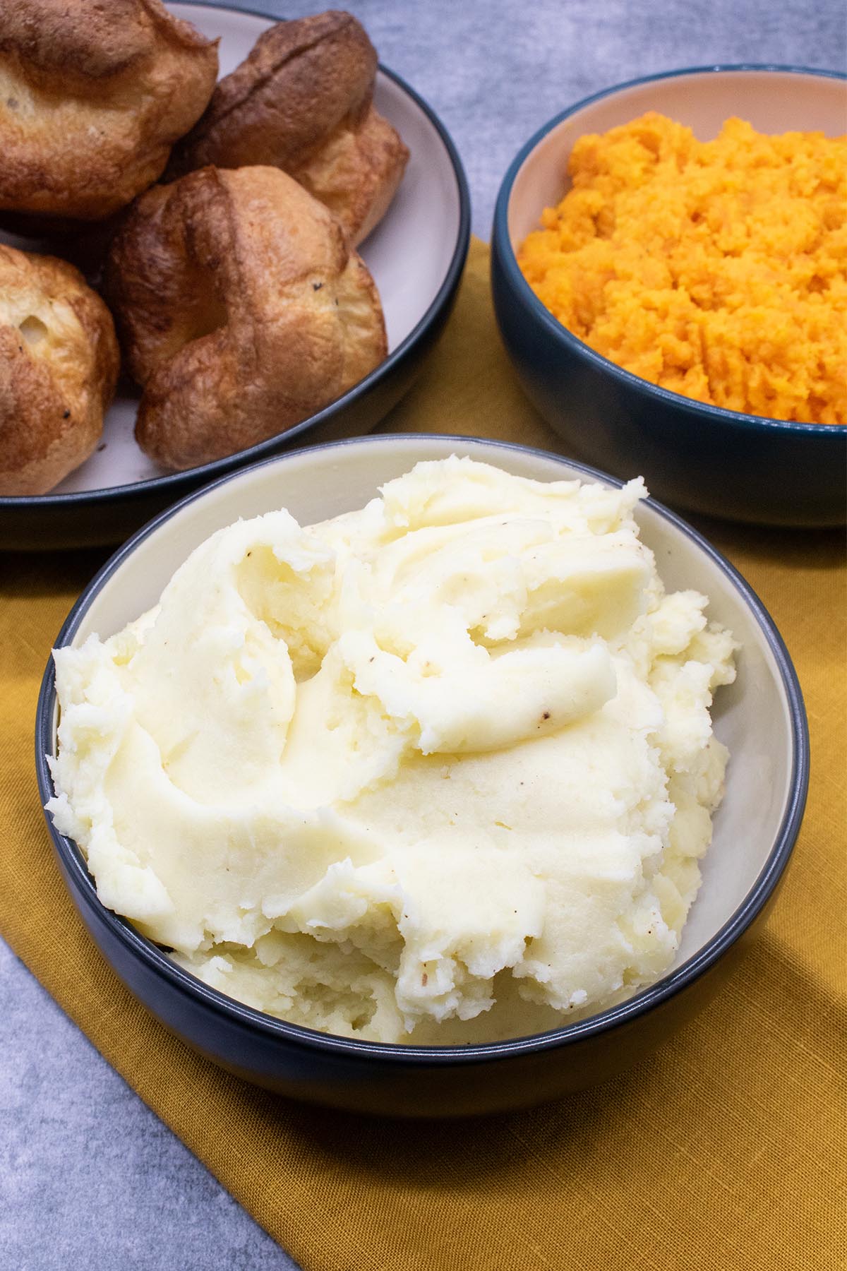 Mashed potatoes in a bowl with Yorkshire puddings and carrot and swede mash in background