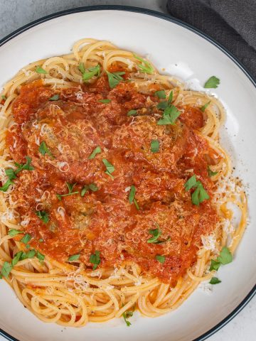 Meatballs with tomato sauce and spaghetti in a pasta bowl, garnished with parmesan and parsley