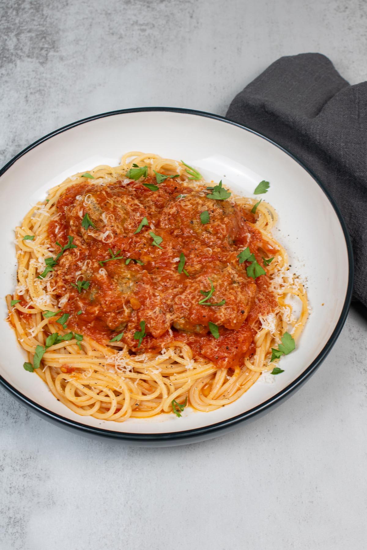 Meatballs with tomato sauce and spaghetti in a pasta bowl, garnished with parmesan and parsley