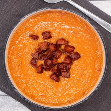 Red lentil and chorizo soup in bowl with fried chorizo topping, sitting on grey napkin