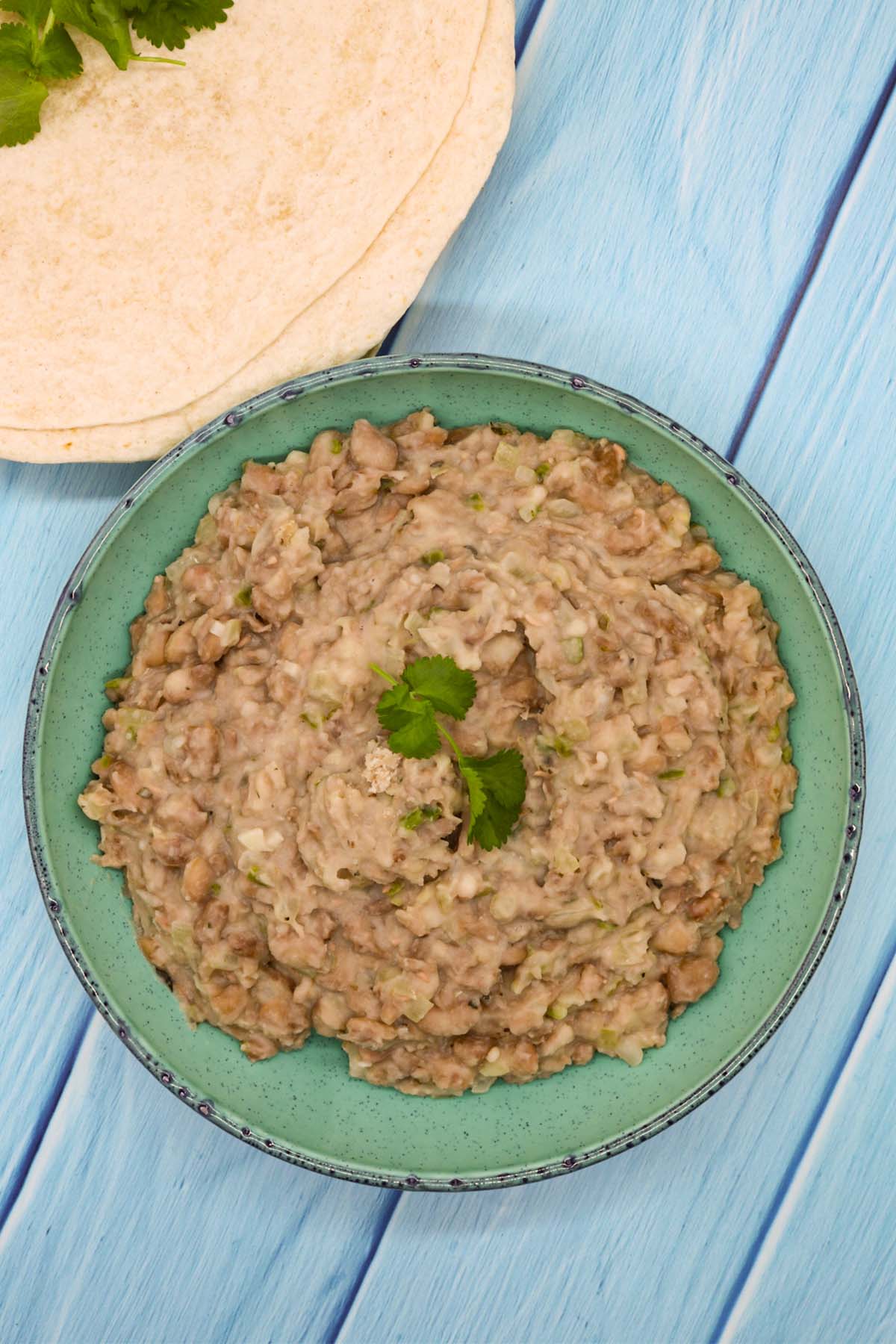 Refried bean in green bowl with flour tortillas in background