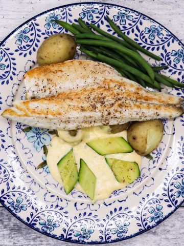 Sea Bass fillet on a blue and white plate with lemony sauce, boiled new potatoes, green beans and courgette