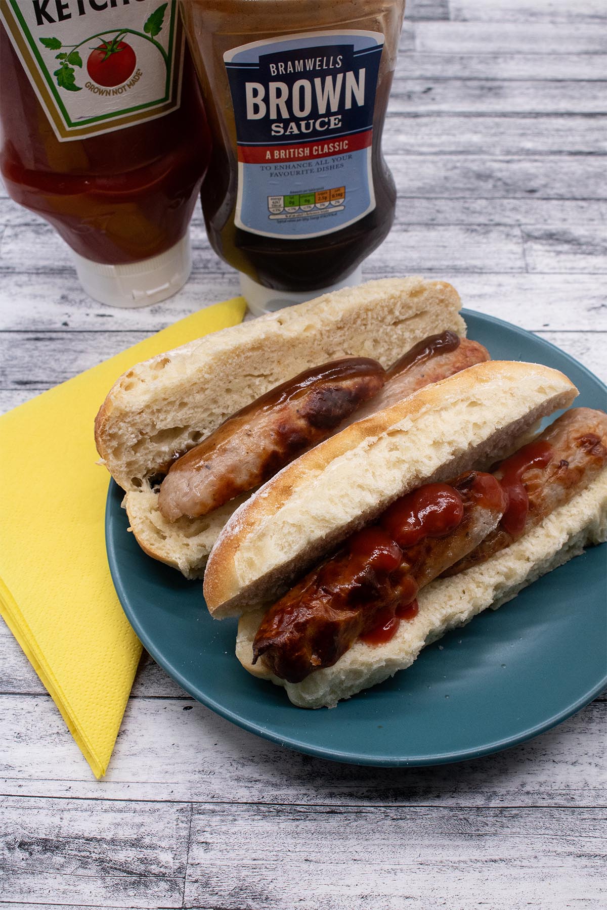 Sausages in side and white finger roll with tomato and brown sauce and sauce bottles