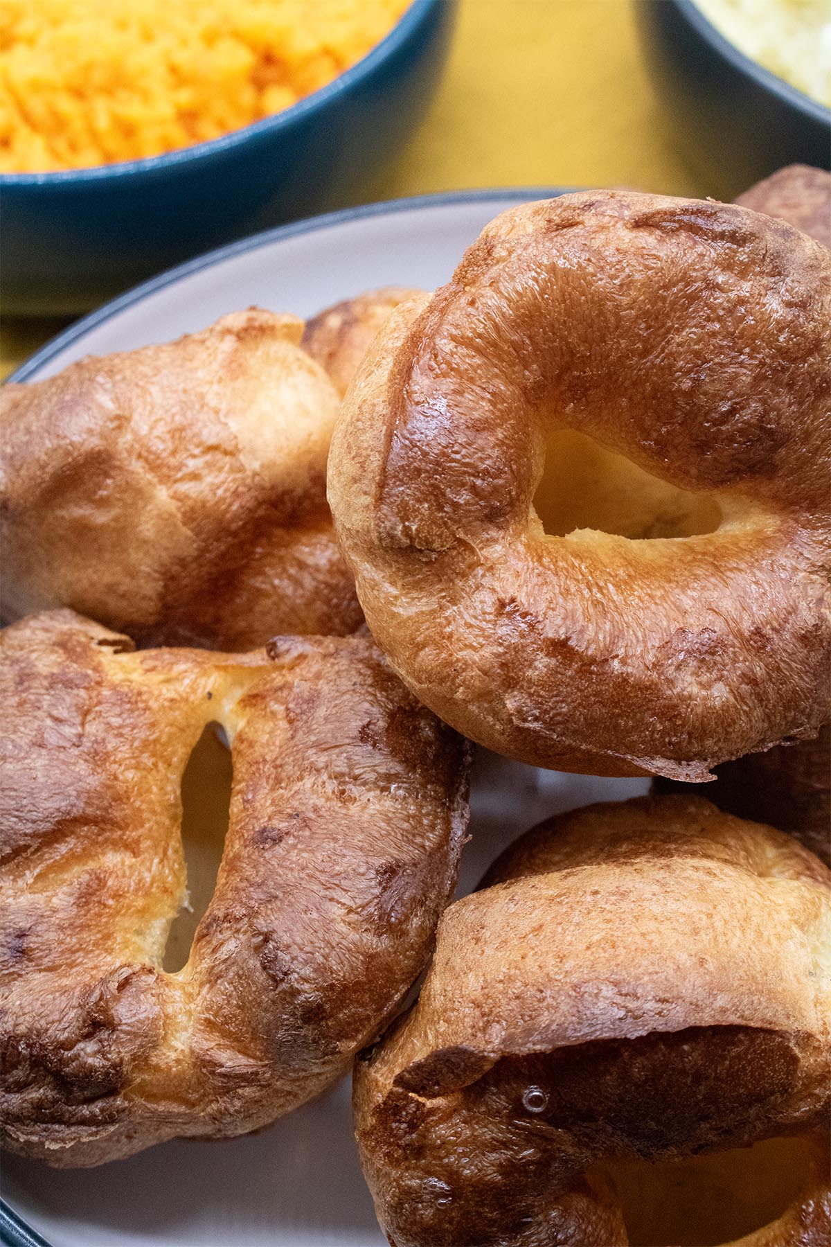 close up of Yorkshire puddings in a white bowl with sides in background
