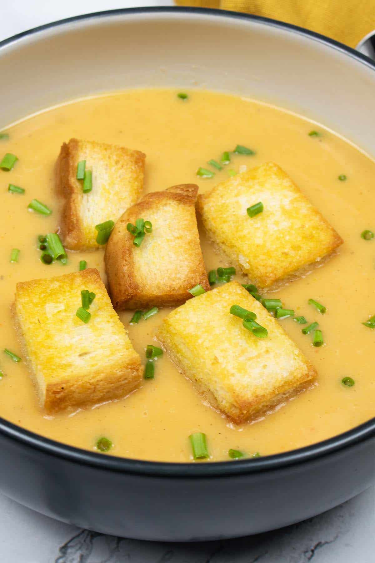 Close up of curried parsnip and sweet potato soup with croutons in a black rimmed bowl.