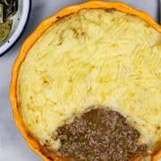 Shepherd's pie in a round yellow and blue pie dish with a portion of potatoes removed.