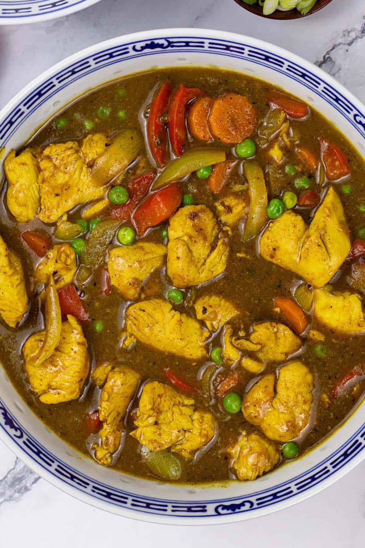Close up of fakeaway Chinese chicken curry in a blue and white oriental serving bowl.