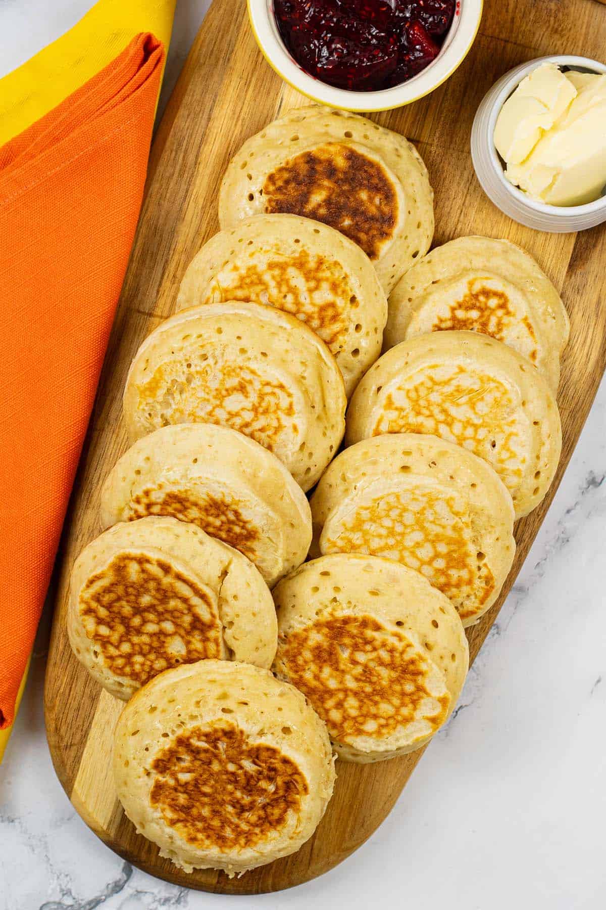 Homemade crumpets on a board with dishes of jam and butter.
