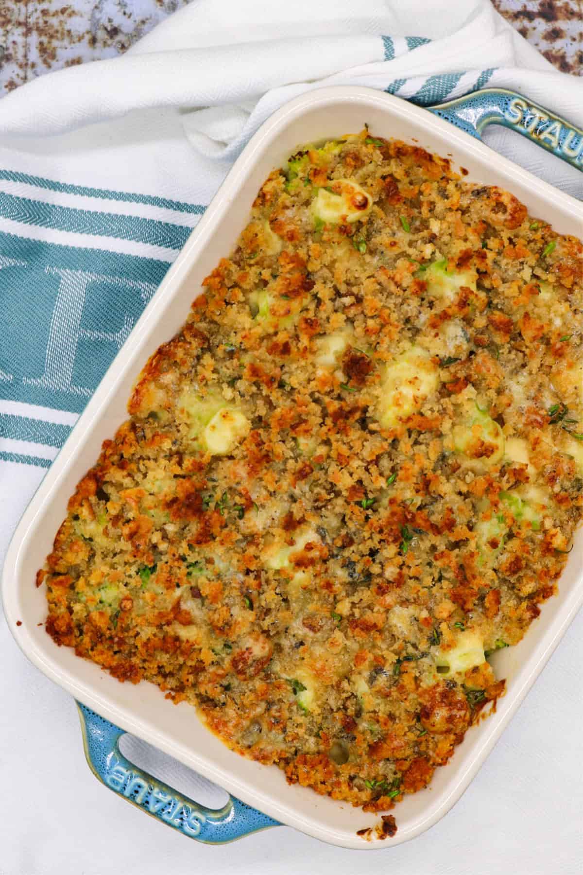 Broccoli and stilton crumble in a rectangle Staub oven dish sitting on a white and teal towel.