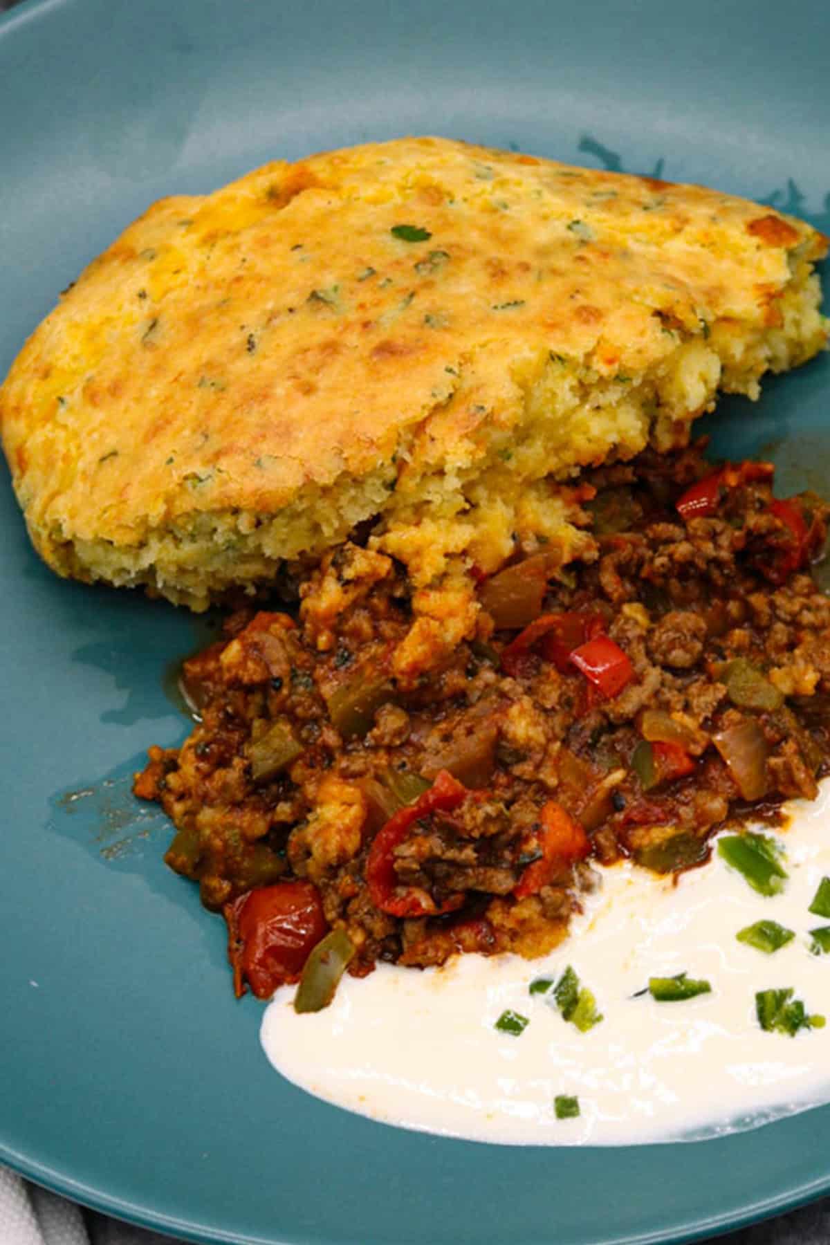 A portion of chilli cornbread pie on a teal dinner plate with some sour cream on the side.