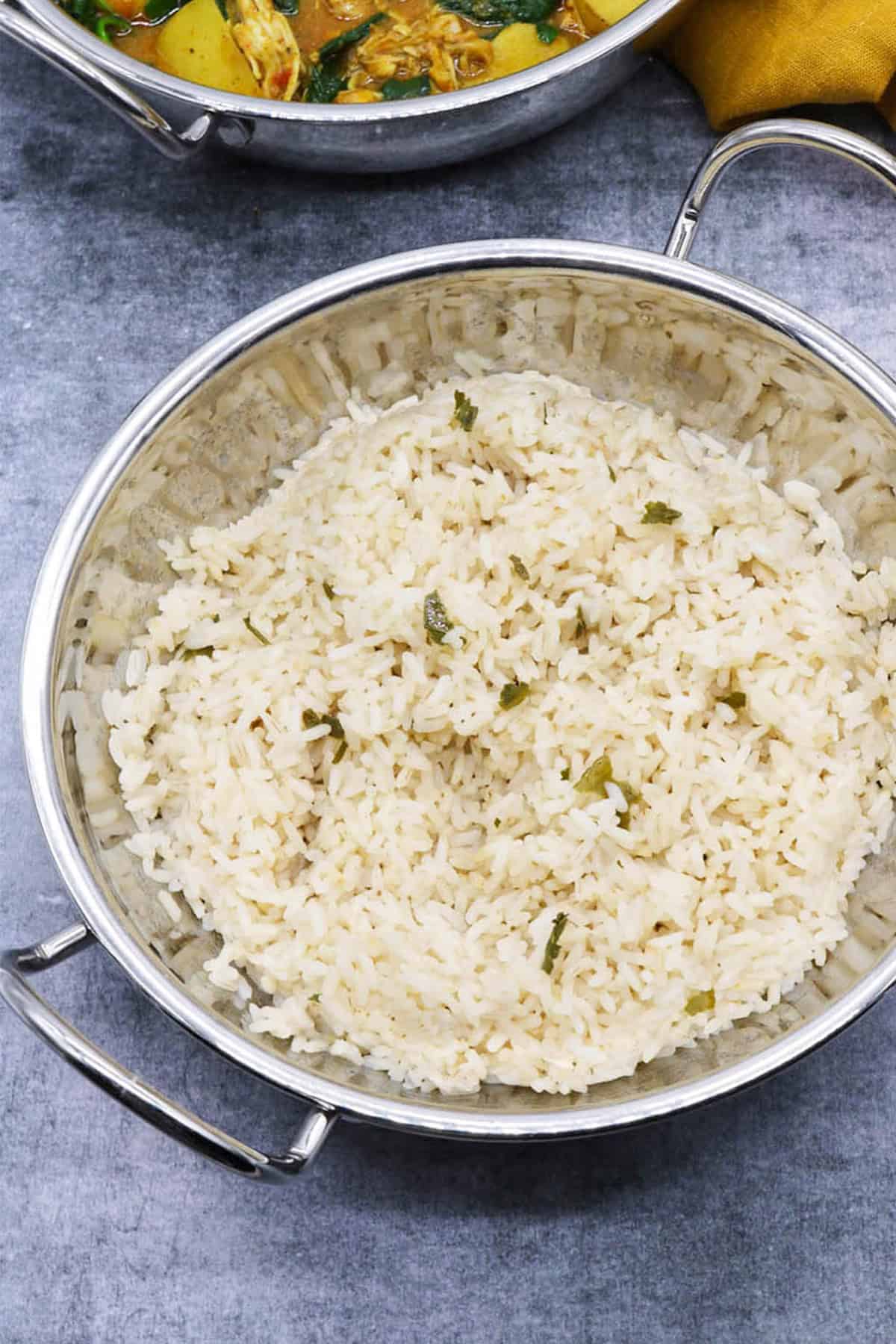 Coconut rice in a balti dish with a curry in another balti dish in the background.