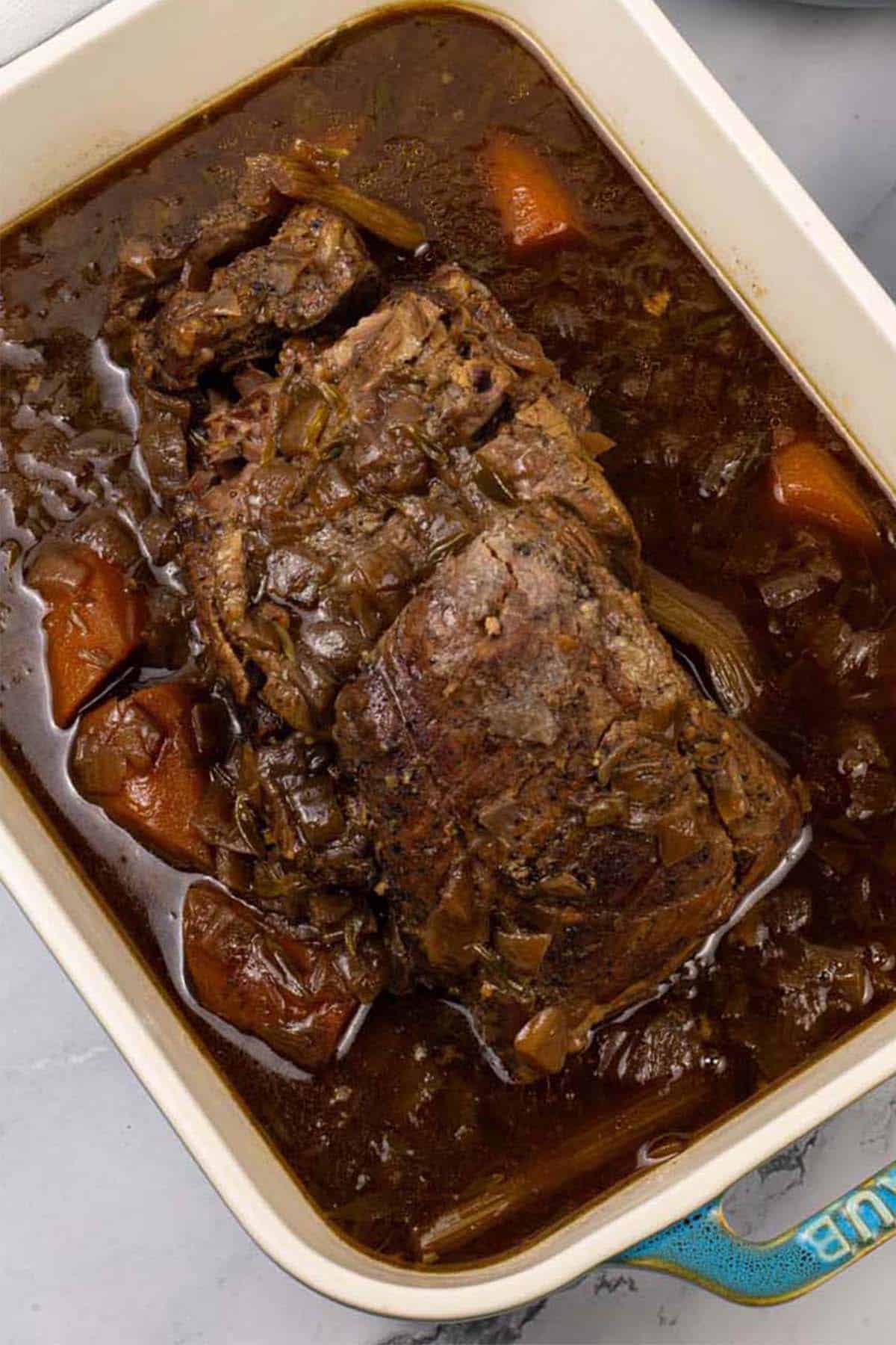 Slow cooked brisket with red wine, thyme and onions in a rectangular serving dish.