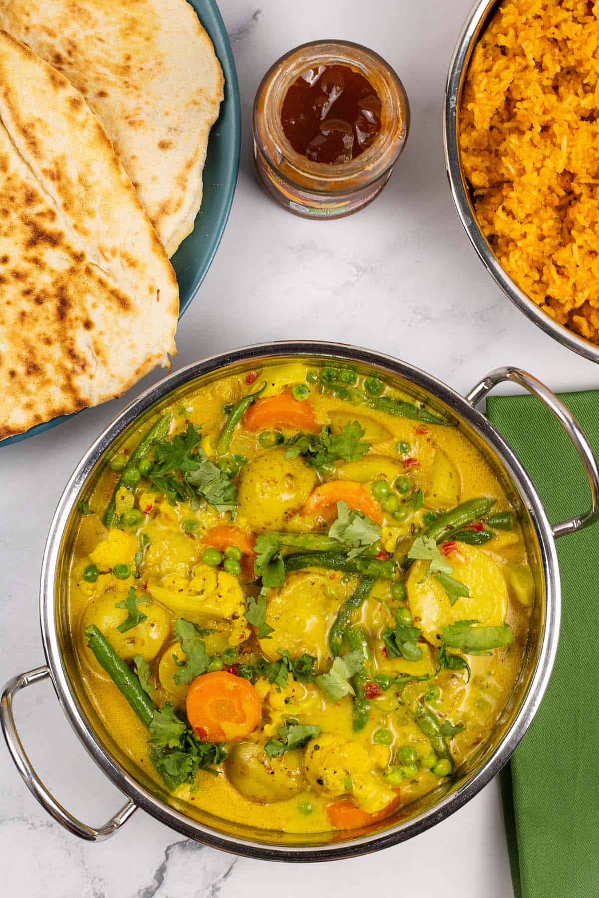Easy Indian vegetable curry in a balti dish with red lentils and rice, mango chutney and quick naan breads in the background.