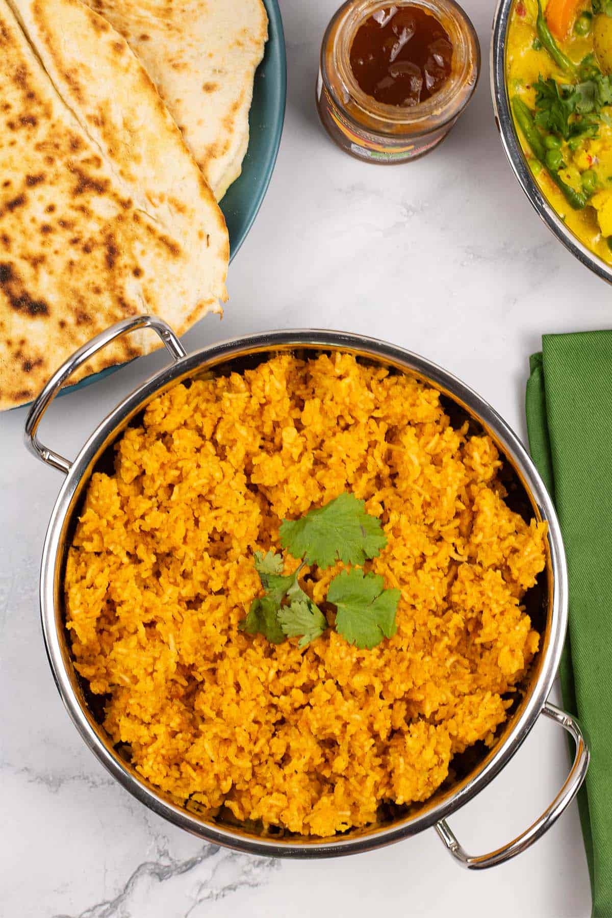 Red lentils and rice in a balti dish with quick naan breads, mango chutney and vegetable curry in the background.