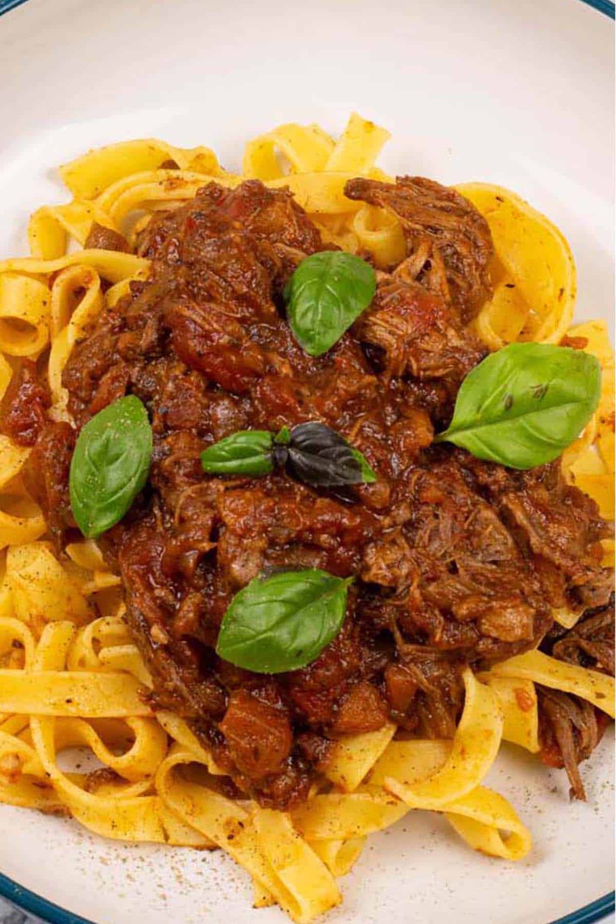 Close up of a portion of slow cooker beef ragu in a pasta bowl with tagliatelle.