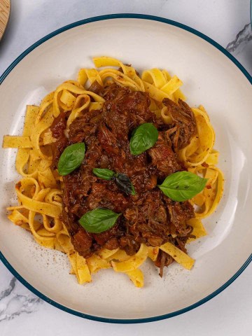 A portion of slow cooker beef ragu in a pasta bowl with tagliatelle.