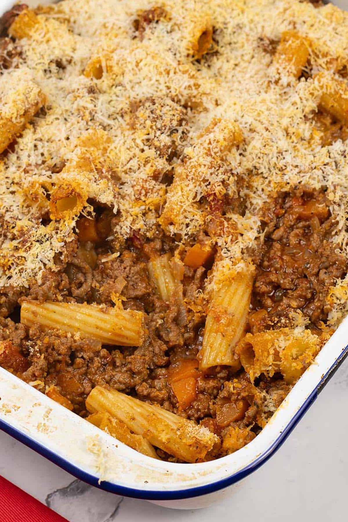 Close up photo of beef and tomato pasta bake in a blue rimmed white enamel roasting tin.