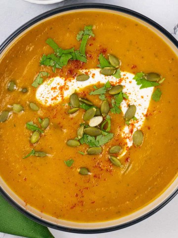 A bowl of carrot and coriander soup with a dark green napkin on the side.