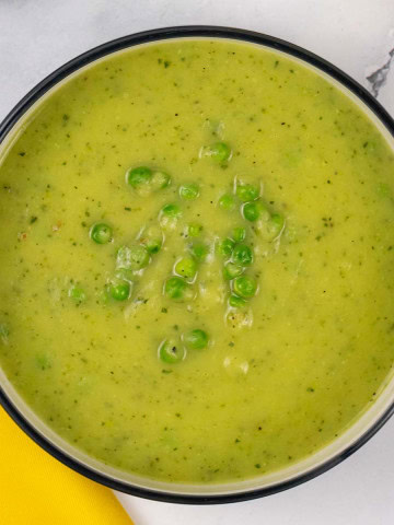Courgette, potato and leek soup in a black and cream bowl.