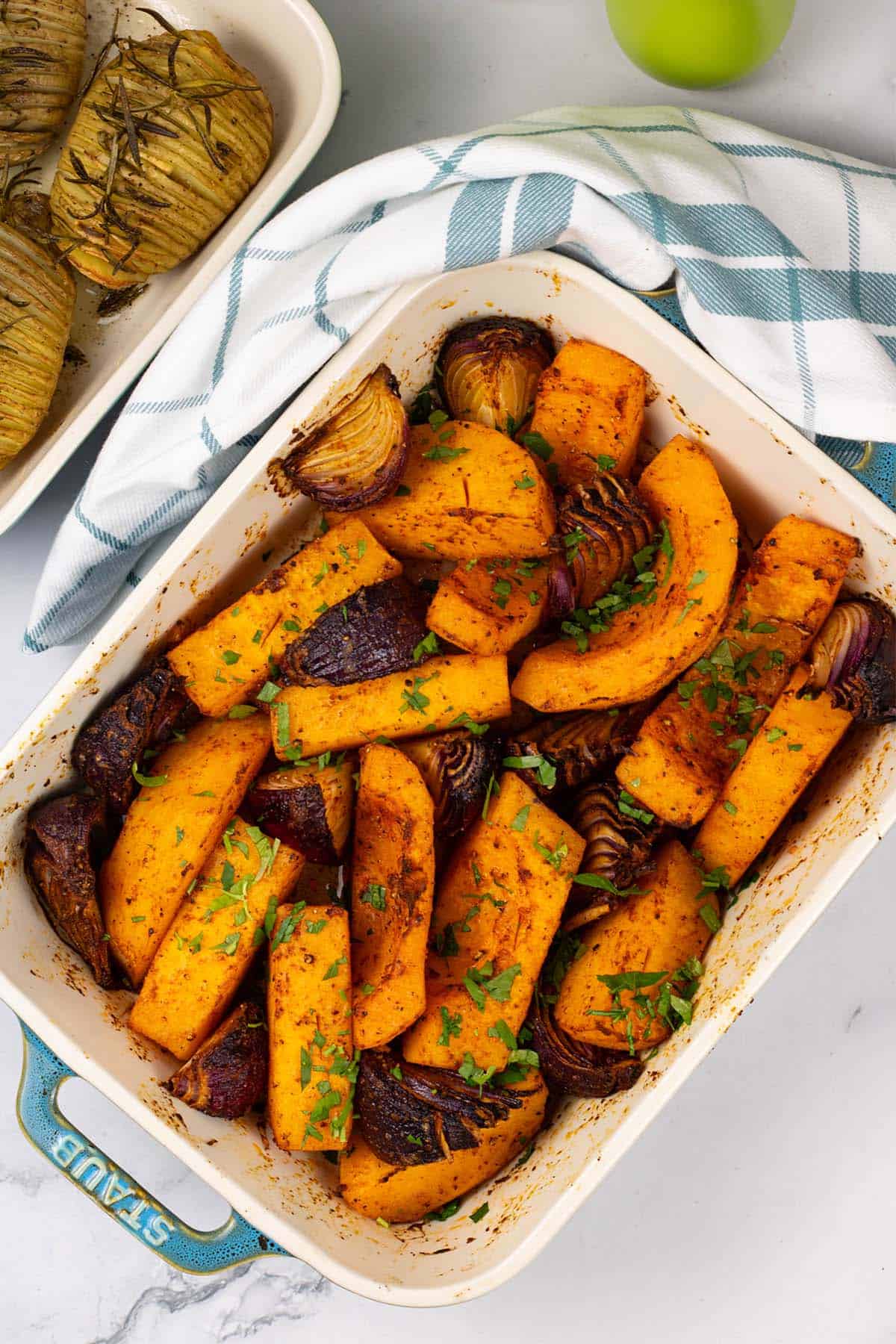 Roast paprika squash and red onions in a rectangle Staub ovenproof dish with a teal and white check towel.