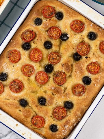 Tomato and olive focaccia in a blue rimmed white enamel roasting tin.