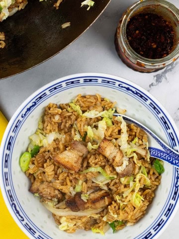 A portion of Cantonese pork belly fried rice in a blue and white oriental bowl with the wok in the background.