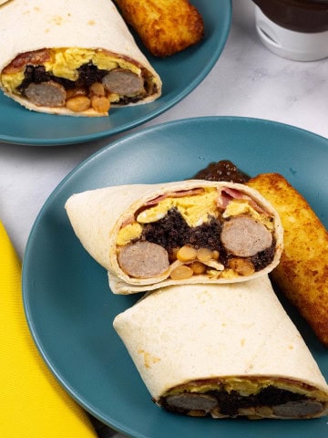 Two portions of breakfast burritos on teal side plates with a cheesy hash brown and blob of brown sauce on the side.