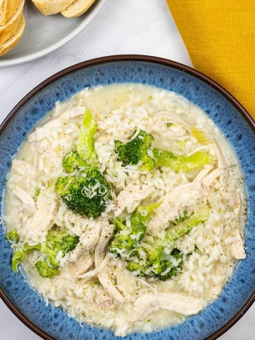 Chicken and broccoli risotto in a blue patterned bowl with a plate of sliced baguette and a mustard napkin on the side.