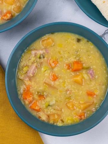 Two portions of lentil soup in teal bowls with sliced bread on the side.