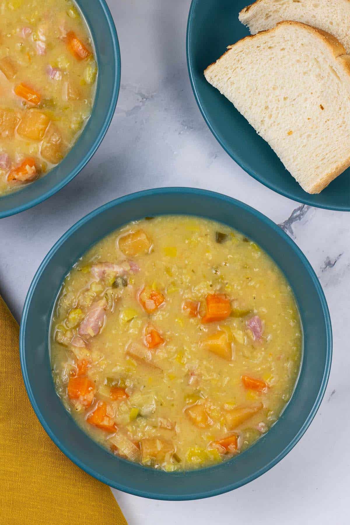 Two portions of lentil soup in teal bowls with sliced bread on the side.