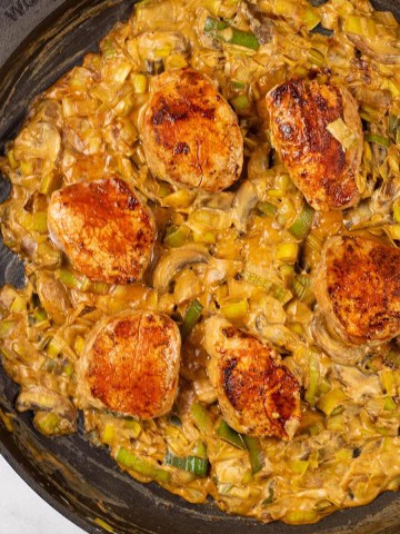 Pork fillet with mushroom and leek sauce in a large frying pan.