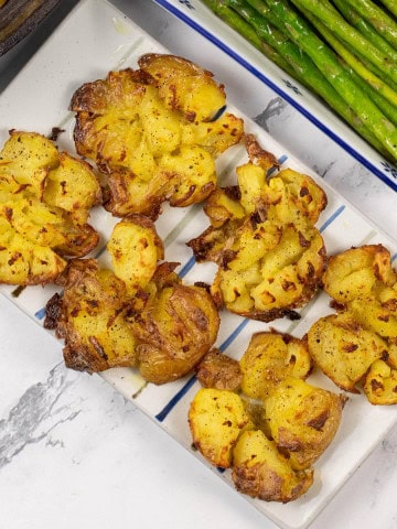 Roast smashed baby potatoes on a white striped platter.