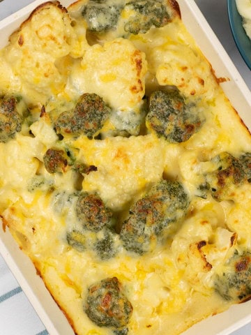 Cauliflower and broccoli cheese in a rectangle Staub oven dish with a bowl of mashed potatoes on the side.