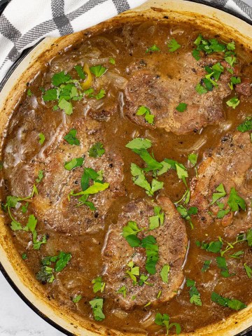 Cider braised pork steaks with onions in a large shallow round casserole.