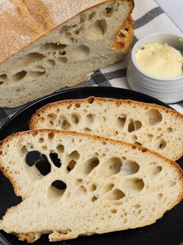 Portuguese water bread made in the Thermomix on a black and white checked towel, with a couple of slices on a black side plate.