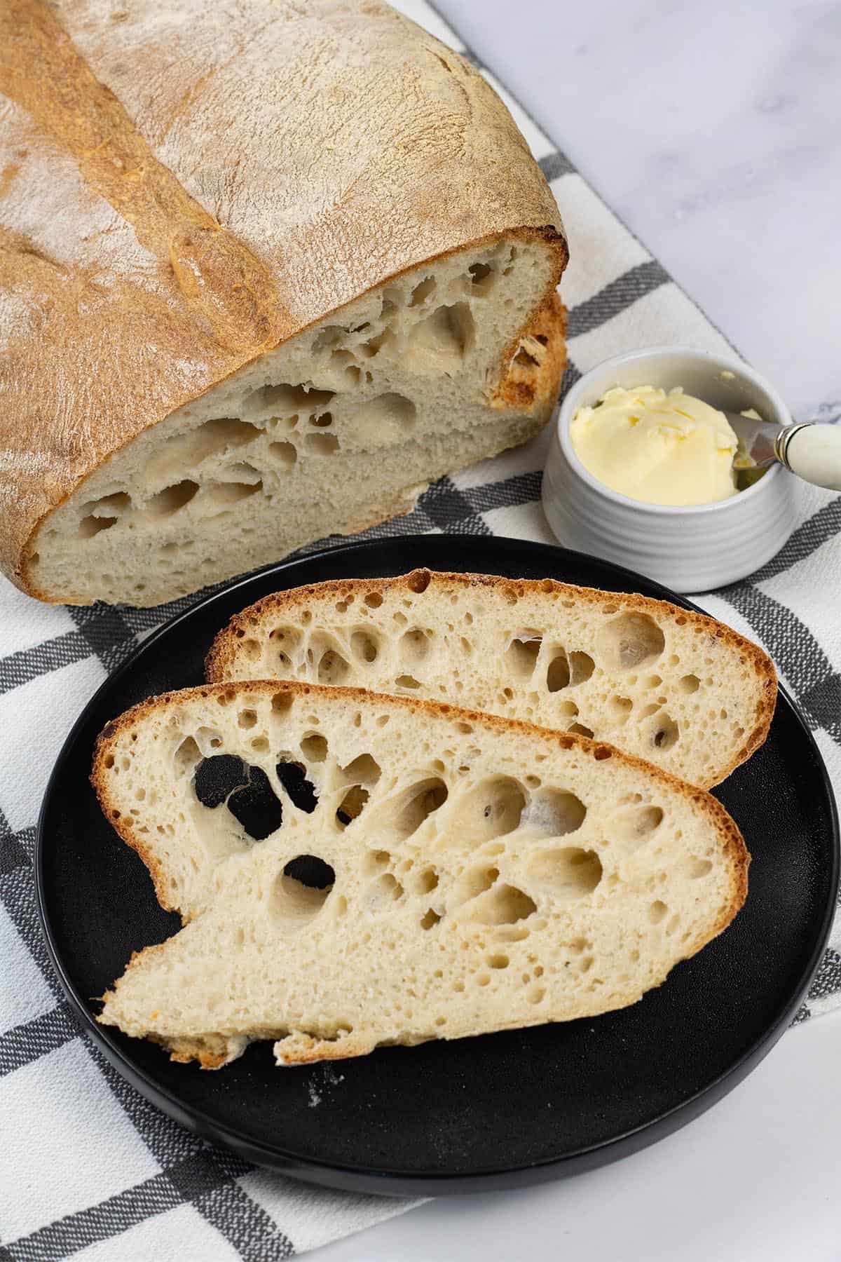 Portuguese water bread made in the Thermomix on a black and white checked towel, with a couple of slices on a black side plate.