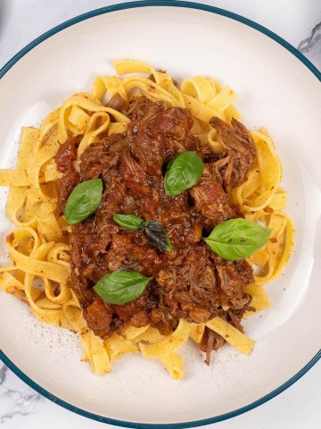 A portion of slow cooker beef ragu in a pasta bowl with tagliatelle.