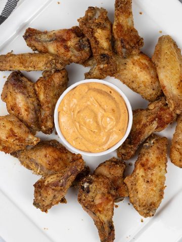 Easy air fryer cajun chicken wings on a white square platter with a dish of cajun dipping sauce.